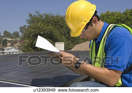 Stock Photo - Maintenance worker makes notes with solar array on rooftop, Los Angeles, California. Fotosearch