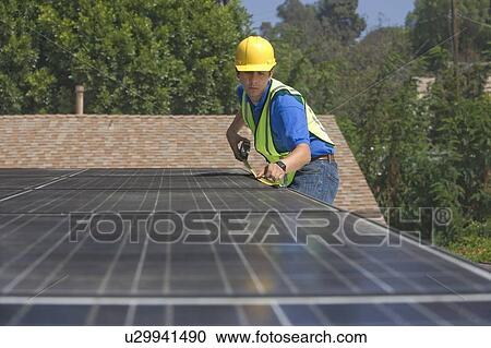 Stock Image - Maintenance worker measures solar array on rooftop, Los Angeles, California. Fotosearch