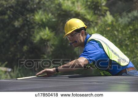 Stock Photo - Maintenance worker measures solar array on rooftop, Los Angeles, California. Fotosearch