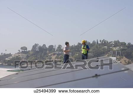 Stock Photo - Maintenance workers stand with solar array on rooftop in Los Angeles, California. Fotosearch