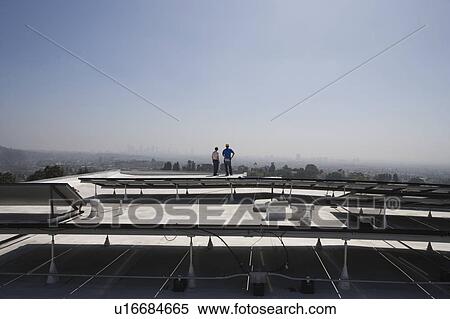 Stock Photography - Maintenance workers stand with solar array on rooftop in Los Angeles, California. Fotosearch