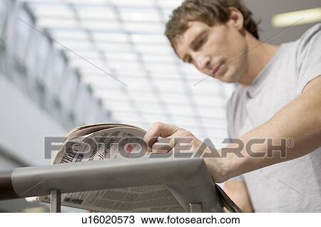 Stock Image - Young man stands reading newspaper in new shopping centre, Voronezh. Fotosearch