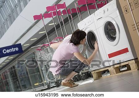 Stock Photography - Young woman looks inside tub of washing machine in shopping mall, Voronezh. Fotosearch