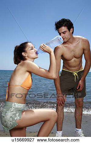 Athletic couple on the beach; female drinking bottled water View Large Photo Image Stock Photo - Athletic couple on the beach; female drinking bottled water. Fotosearch
