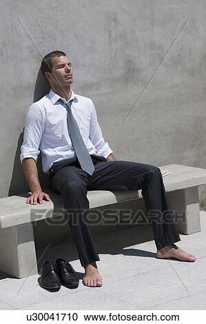 Stock Image - Barefoot businessman sitting on bench enjoying the sun. Fotosearch