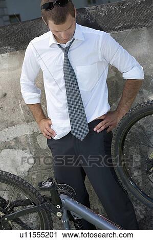 Stock Image - Businessman in suit next to broken bicycle. Fotosearch