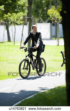 Stock Image - Businessman in suit riding bike. Fotosearch