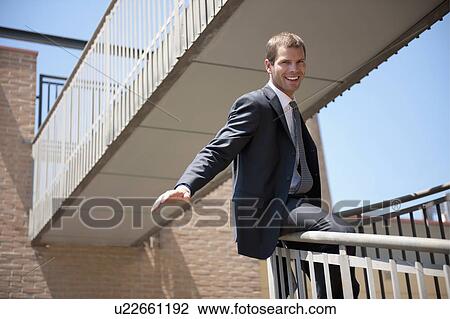 Stock Image - Businessman in suit sliding down bannister. Fotosearch