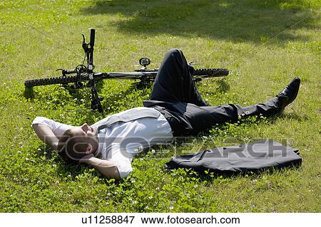 Businessman lying down in grass next to bicycle enjoying the sun View Large Photo Image Stock Photo - Businessman lying down in grass next to bicycle enjoying the sun. Fotosearch