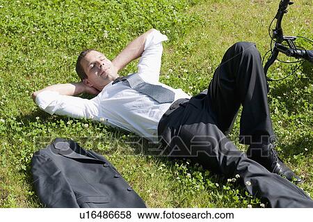 Businessman lying down in grass next to bicycle enjoying the sun View Large Photo Image Stock Photo - Businessman lying down in grass next to bicycle enjoying the sun. Fotosearch