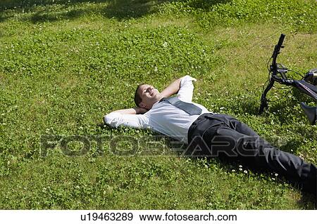 Stock Photo - Businessman lying down in grass next to bicycle enjoying the sun. Fotosearch