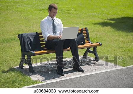 Businessman sitting on bench with laptop View Large Photo Image Stock Image - Businessman sitting on bench with laptop. Fotosearch