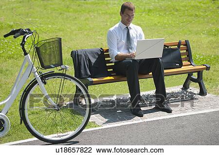 Businessman sitting on bench with laptop and bicycle View Large Photo Image Stock Image - Businessman sitting on bench with laptop and bicycle. Fotosearch