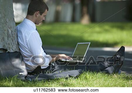 Businessman with laptop working under a tree View Large Photo Image Stock Image - Businessman with laptop working under a tree. Fotosearch