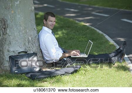 Stock Image - Businessman with laptop working under a tree. Fotosearch