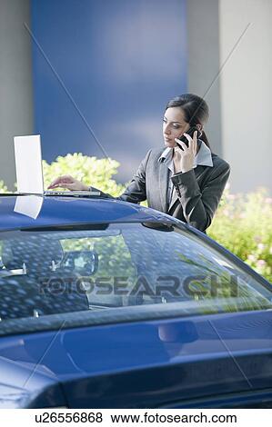 Businesswoman next to car with laptop talking on smartphone View Large Photo Image Stock Photo - Businesswoman next to car with laptop talking on smartphone. Fotosearch