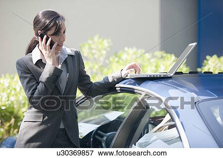 Businesswoman next to car with laptop talking on smartphone View Large Photo Image Stock Photo - Businesswoman next to car with laptop talking on smartphone. Fotosearch