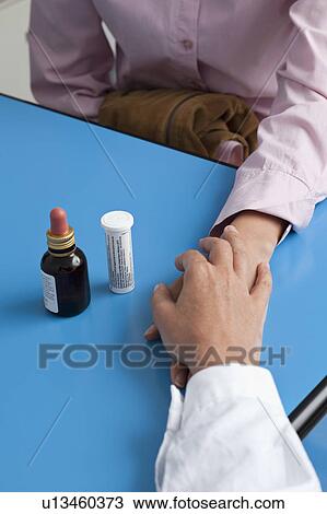 Stock Image - Closeup of doctor's hand holding patient's hand with medicine on table. Fotosearch
