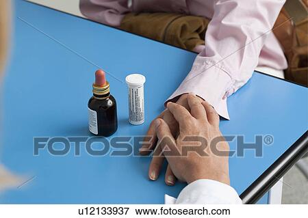 Stock Photo - Closeup of doctor's hand holding patient's hand with medicine on table. Fotosearch