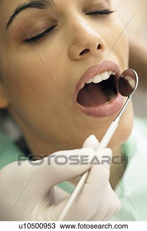 Stock Image - Closeup of patient's face and dentist's hand holding mirror. Fotosearch