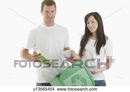 Picture - Couple throwing glass and plastic bottles in the recycling bin. Fotosearch