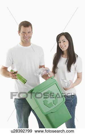 Stock Photo - Couple throwing glass and plastic bottles in the recycling bin. Fotosearch