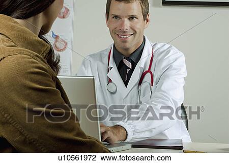 Stock Image - Doctor at laptop with patient in office. Fotosearch