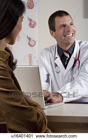 Stock Image - Doctor at laptop with patient in office. Fotosearch