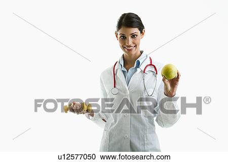 Stock Image - Doctor holding apple and hand weights. Fotosearch