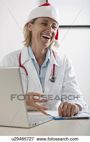 Stock Photo - Doctor laughing wearing Santa's hat. Fotosearch