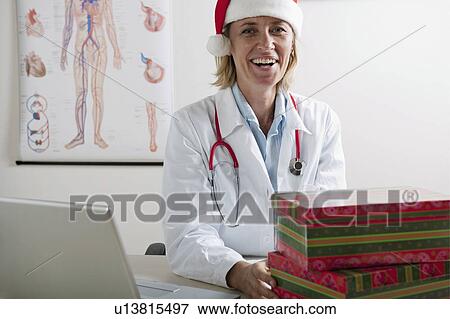 Doctor laughing with presents and laptop View Large Photo Image Stock Photo - Doctor laughing with presents and laptop. Fotosearch
