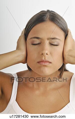 Stock Image - Female young adult; hands holding ears; eyes closed. Fotosearch