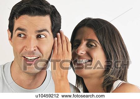 Stock Image - Female young adult whispering in man's ear. Fotosearch