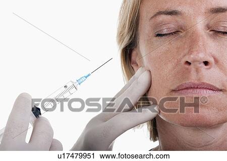 Stock Image - Hand holding botox syringe to woman's face. Fotosearch