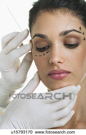 Stock Image - Hands with surgical gloves on patient's face with distance marker. Fotosearch