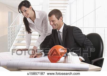 Stock Photo - Man and woman looking over plans at desk. Fotosearch