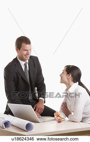 Stock Photograph - Man and woman with plans and laptop at desk. Fotosearch