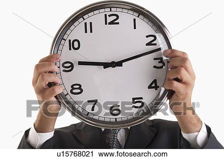 Stock Image - Man holding clock in front of his face. Fotosearch