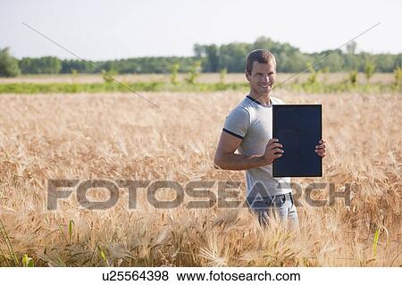 Stock Photo - Man holding solar panel in wheat field. Fotosearch