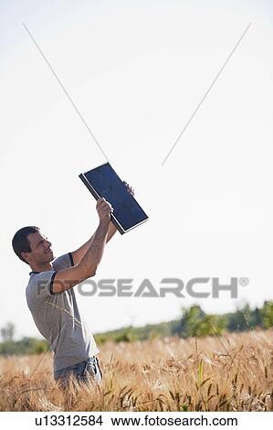 Picture - Man holding up solar panel in wheat field. Fotosearch