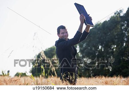 Man in suit holding up solar panel in wheat field View Large Photo Image Picture - Man in suit holding up solar panel in wheat field. Fotosearch
