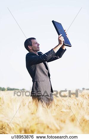 Stock Photograph - Man in suit holding up solar panel in wheat field. Fotosearch