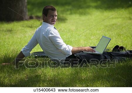 Stock Image - Man sitting in grass with laptop. Fotosearch