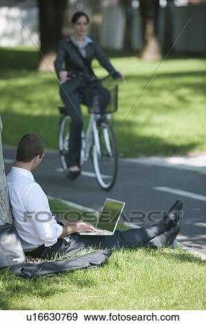 Man sitting under tree with laptop, woman riding bike View Large Photo Image Stock Photo - Man sitting under tree with laptop, woman riding bike. Fotosearch