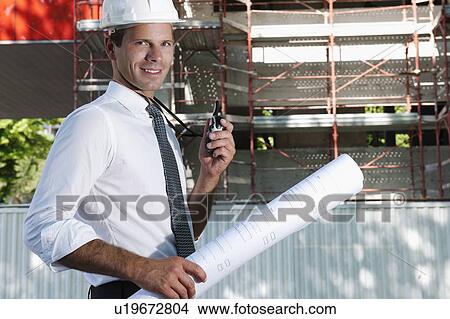 Man with hardhat, walky talky radio, and architectural plans at construction site View Large Photo Image Picture - Man with hardhat, walky talky radio, and architectural plans at construction site. Fotosearch
