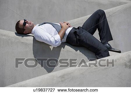 Stock Photo - Man with tie and sunglasses lying down on wall. Fotosearch