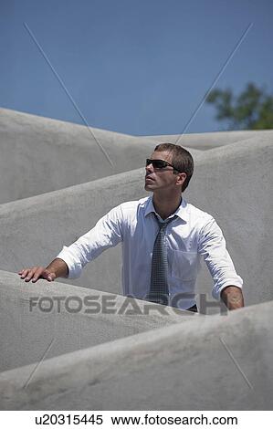 Stock Photography - Man with tie and sunglasses standing behind wall. Fotosearch