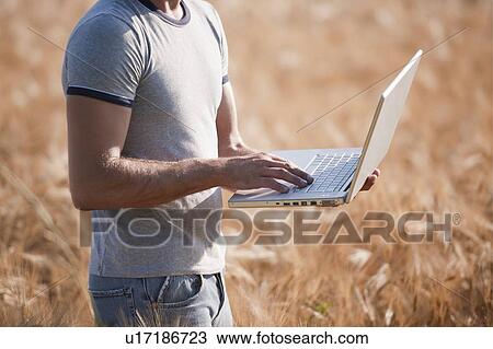 Stock Image - Man's torso with laptop computer in wheat field. Fotosearch