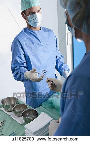 Stock Image - Nurse handing forceps to surgeon in operating room. Fotosearch