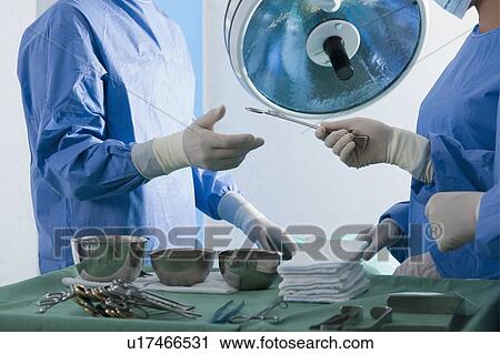 Stock Image - Nurse handing forceps to surgeon in operating room. Fotosearch